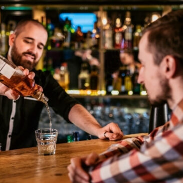 male bartender pouring drink into rocks glass