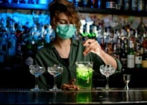 a female bartender making drinks wearing a mask
