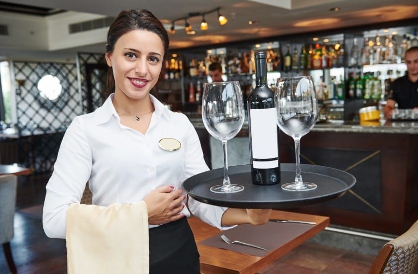 waitress with a bottle of wine and two empty glasses on a serving platter