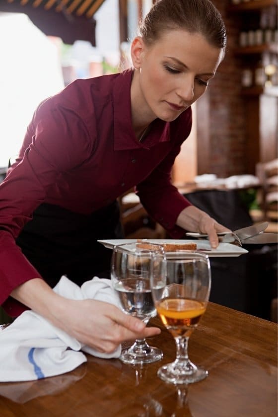 female server picking up drink glasses from the bar