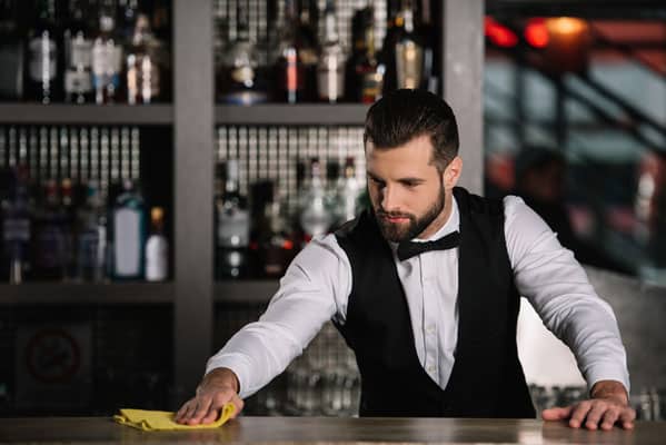 handsome bartender cleaning bar counter in evening