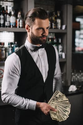happy handsome bartender holding tips at bar
