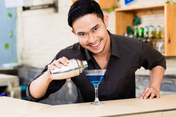 Happy young male bartender making blue margarita cocktail