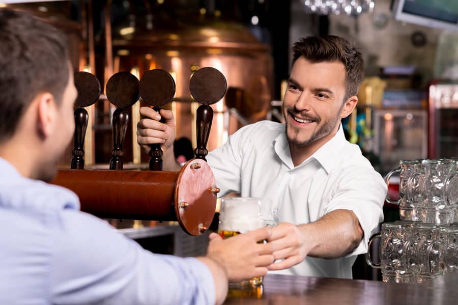Cheerful young bartender giving a mug with beer to the customer