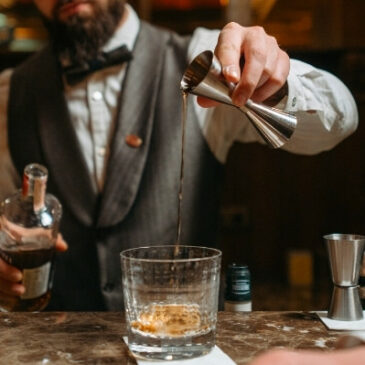 bartender pouring shot into cocktail glass with jigger, bartending 101
