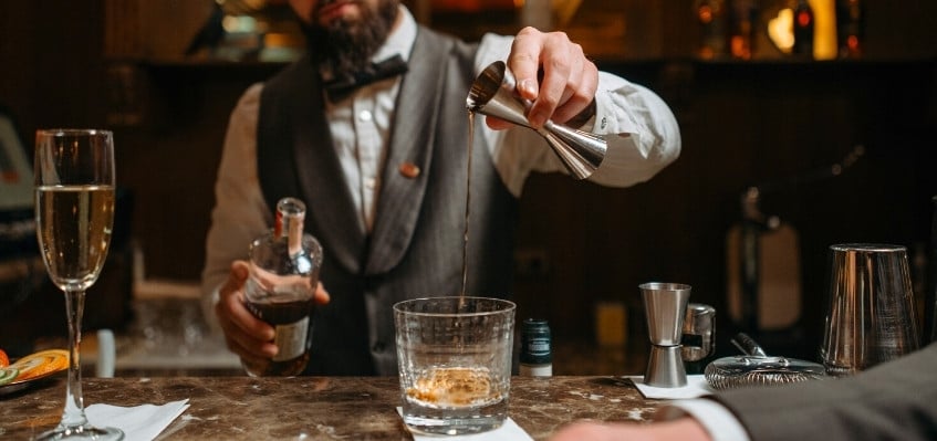 bartender pouring shot into cocktail glass with jigger