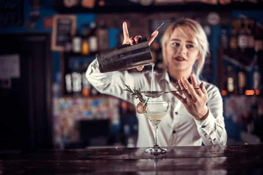 Charismatic girl barman demonstrates the process of making a cocktail while standing near the bar counter in pub