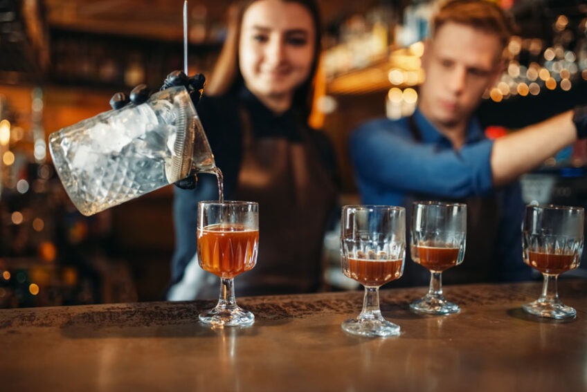 Bartending is a popular profession, Male and female bartender at the bar counter. Alcohol drink preparation. Two barmans working in pub