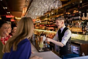 Young bartender making a cocktail for a small group of women enjoying ladies night. They are all laughing and making conversation.