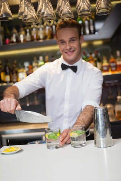 happy bartender adds ice to cocktail
