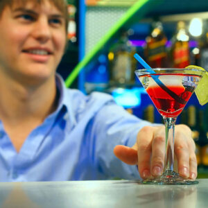 Young bartender makes cocktail in martini glass
