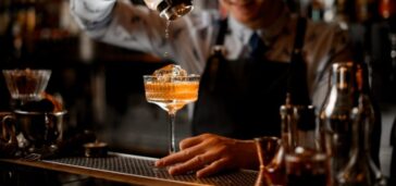 cocktail being poured into glass from shaker by bartender
