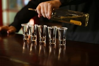 five short glasses being filled by a bartender