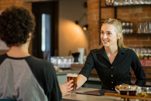 woman handing pint of beer to man at bar counter