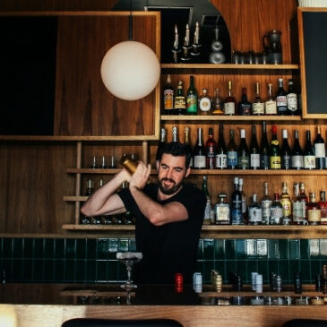 bartender shaking cocktail in shaker behind large wooden bar
