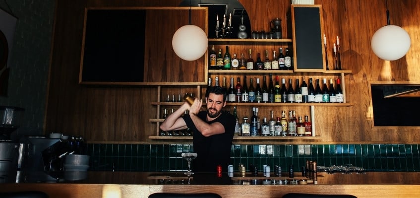 bartender shaking cocktail in shaker behind large wooden bar