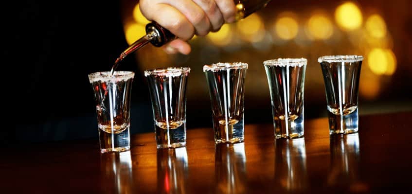 bartender with barandrestaurant pours liquor into five shot glasses