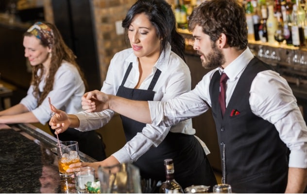 male and female bartender using stirrer to make cocktail, helping bartender make drinks