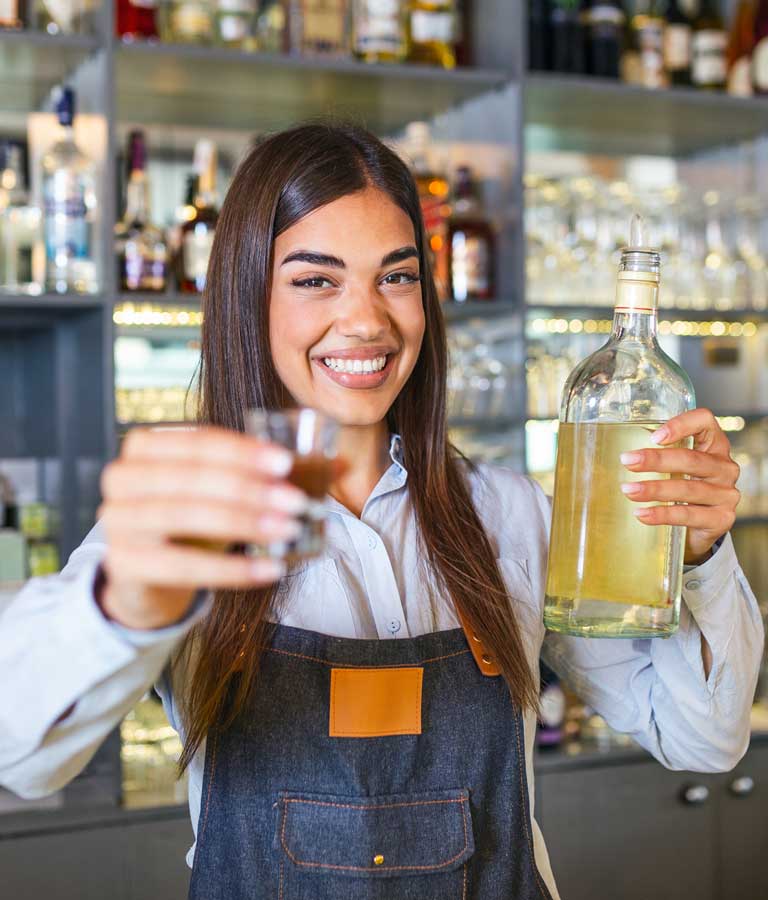 beautiful female bartender is holding a shot glass and bottle