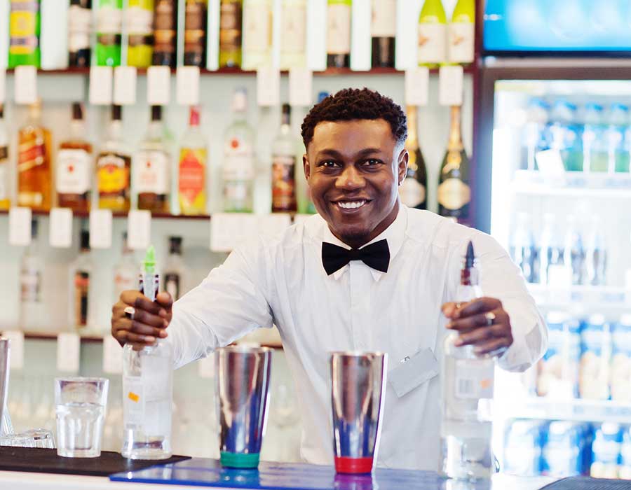 male bartender smiles working the bar with two liquor bottles