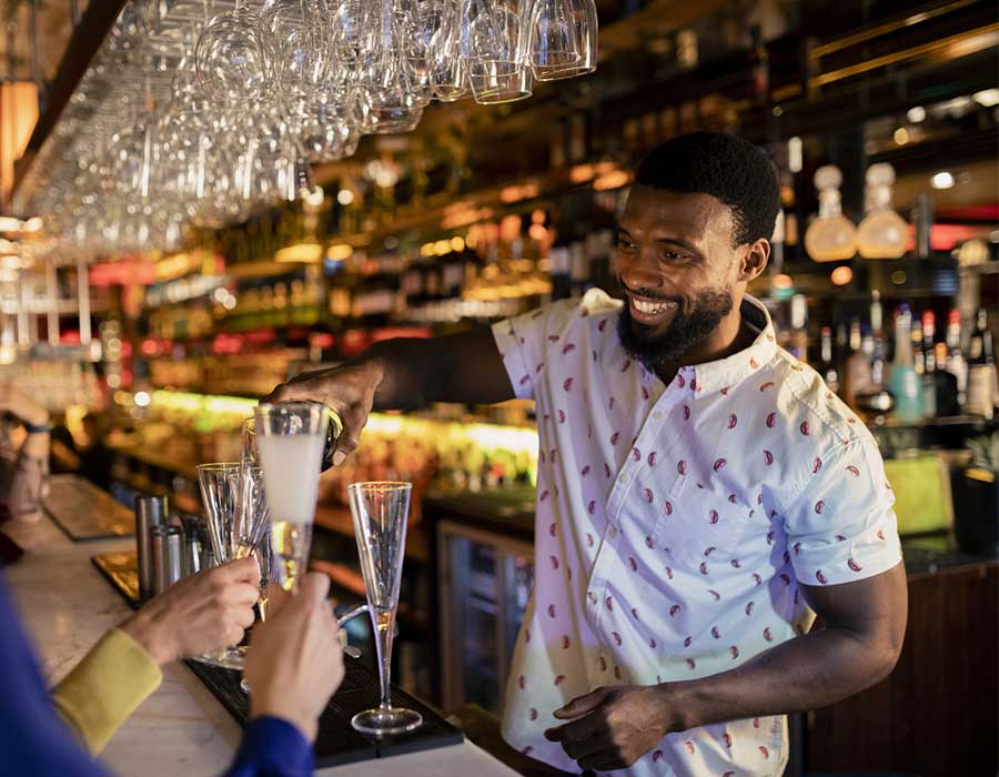 handsome male bartender filling up a flute glass behind bar