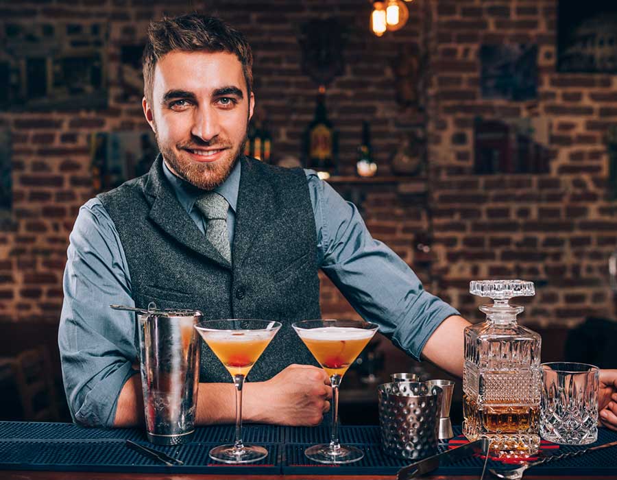 handsome male smiling bartender with two martini glasses behind the bar counter