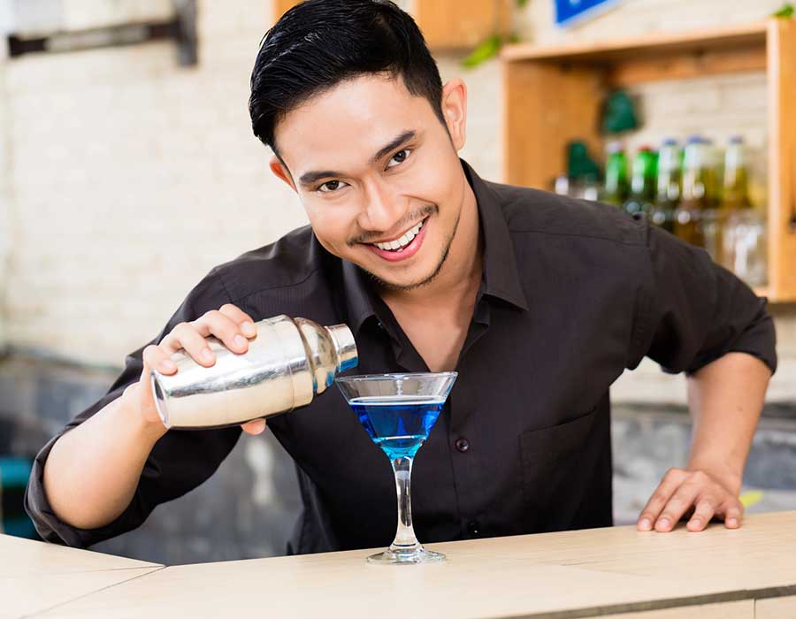 happy young bartender smiles pouring blue margarita