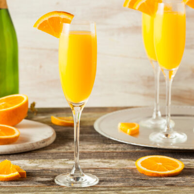 Classic orange juice mimosa in a tall flute with a fresh orange wheel garnish and bubbles