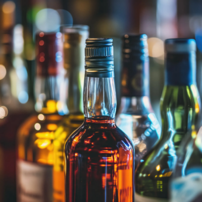 A close-up, shallow depth-of-field shot of several liquor bottles on a bar, with one central bottle of amber spirits in sharp focus.