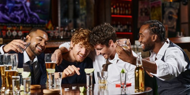 happy and drunk multi-ethnic friends hugging during at bar table
